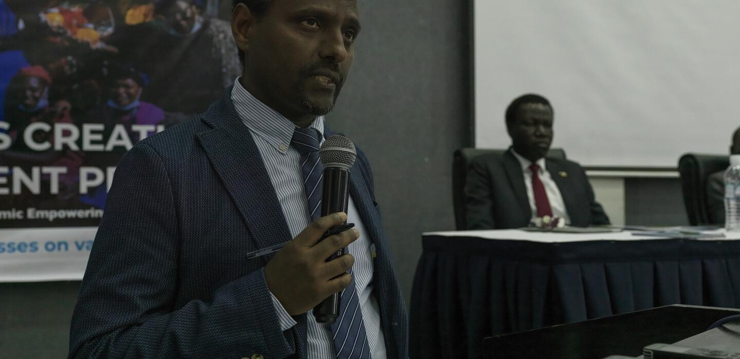 South Sudanese man in business suit stands and speaks into microphone