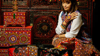 Woman in traditional Turkmen clothing sits in shop of local designs