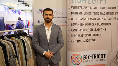 Young Egyptian businessman stands next to display for his textile company