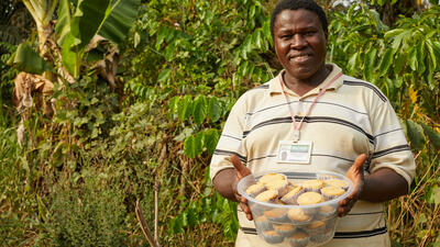 Man in Sierra Leone stands on farm holding bowl of cupcakes