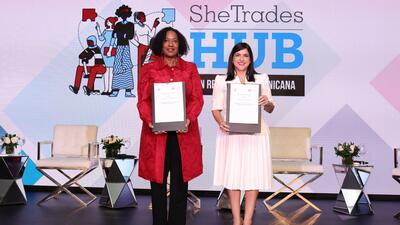 Two women stand on stage holding signed documents