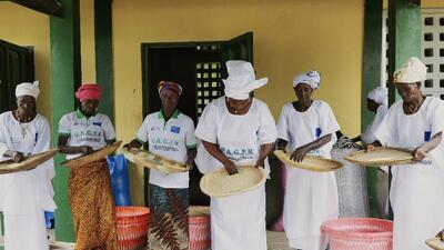 Six Guinean women wearing white hold baskets where they sift rice 