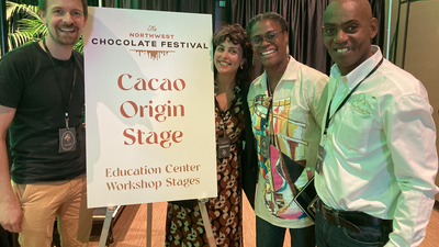 Three people in conference centre stand by sign reading Cacao Origin Stage
