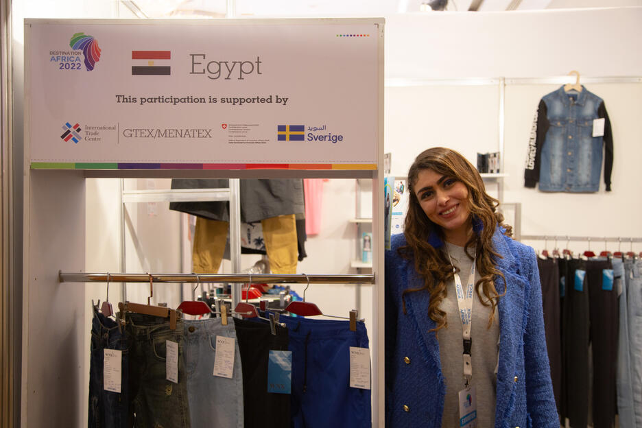 Egyptian woman stands next to clothing display at trade fair.