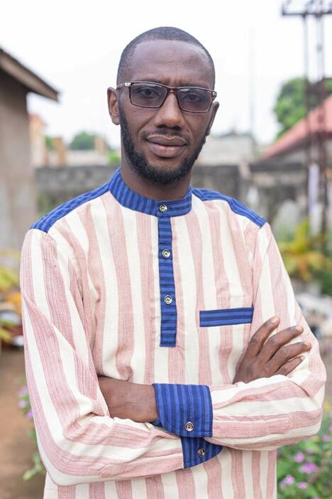Guinean man stands outside in handmade striped shirt
