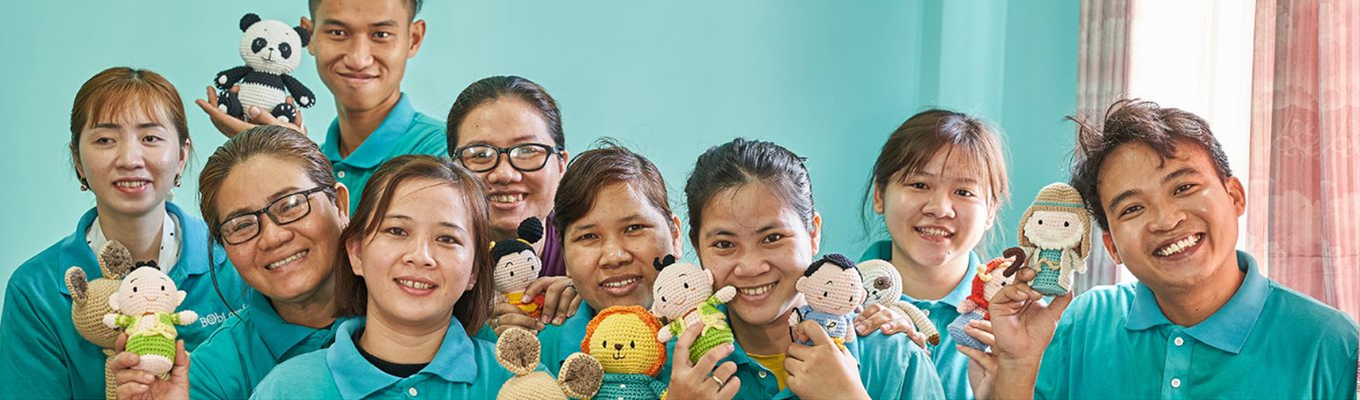 Nine smiling Philippine men and women wearing teal green polo shirts holding stuffed toys