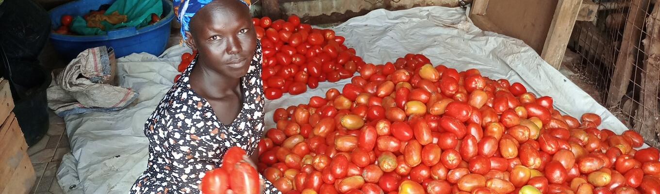 South Sudanese woman sits with phone next to pile of tomatoes at market