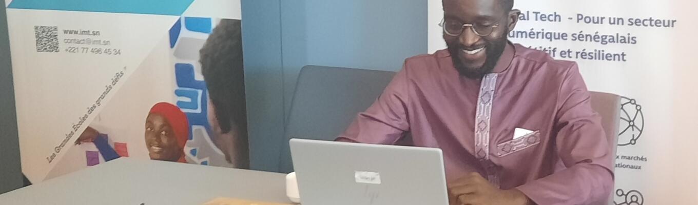 Man sits behind laptop in front of banner for the ITC NTFV Senegal Tech project
