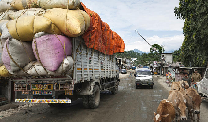 Asian dirt road showing an overladen truck strapped with large bags of grains