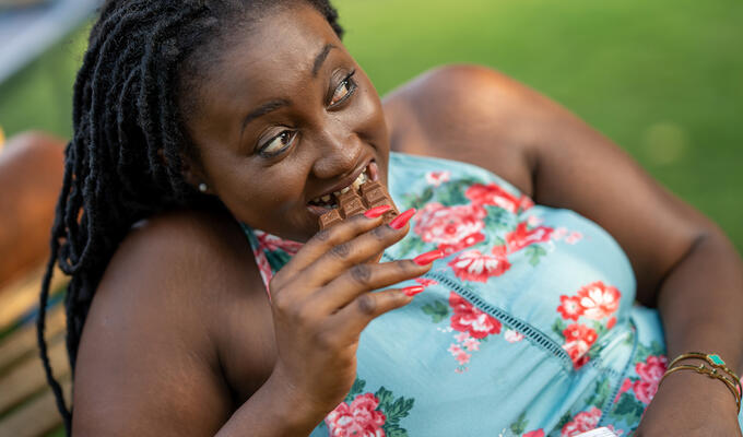 Ghanaian woman in blue floral dress eats chocolate bar