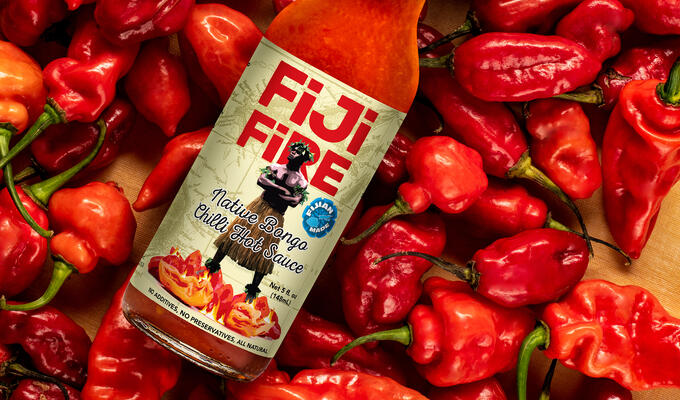 Bottle labelled Fiji Fire rests on a bed of red chilli peppers