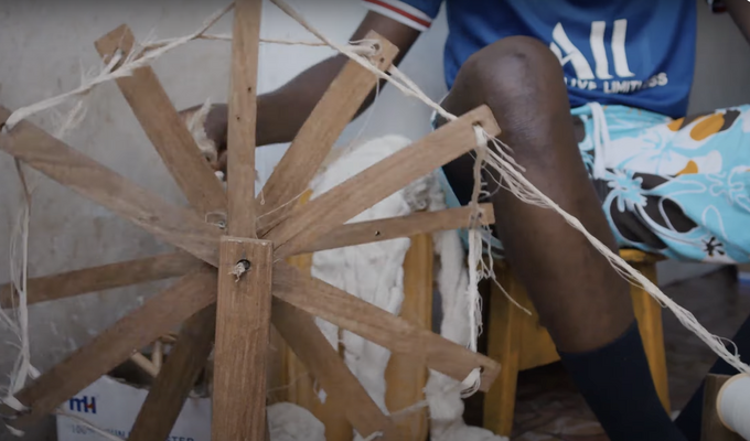 Spinning wheel turns, next to knees of man who is operating it.