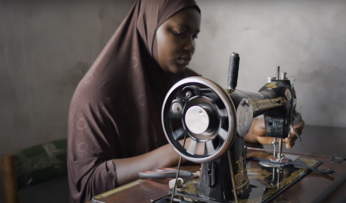 Guinean woman in brown headscarf works at sewing machine