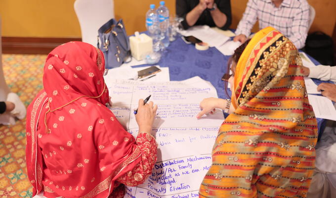 Women in headscarfs huddle around large paper with marker