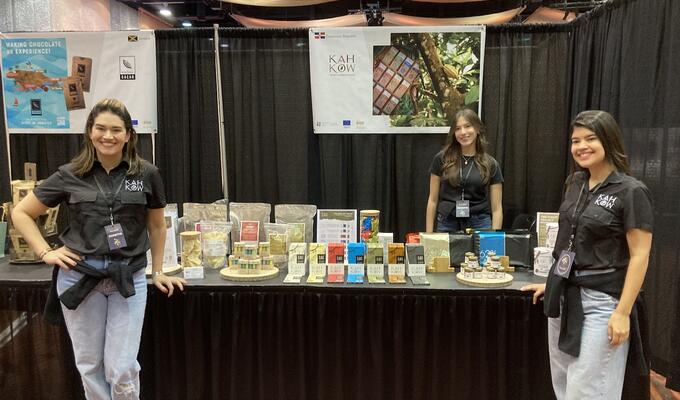 Two women stand next to table displaying Dominican chocolate products