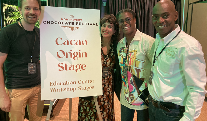 Three people in conference centre stand by sign reading Cacao Origin Stage
