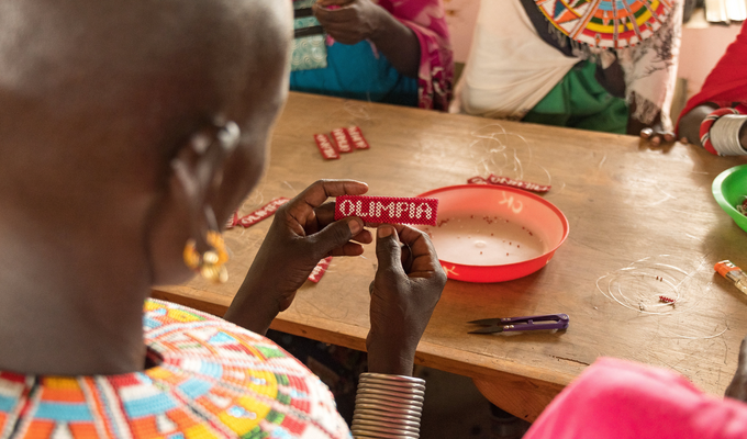 Close-up of Kenyan woman designing beadwork that reads Olimpia