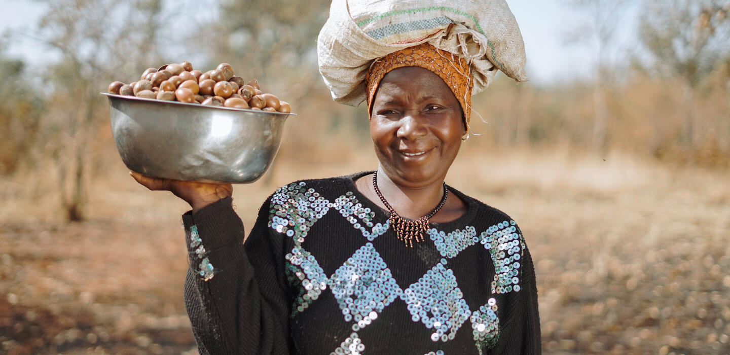 A woman farmer holding shea nuts and smiling.