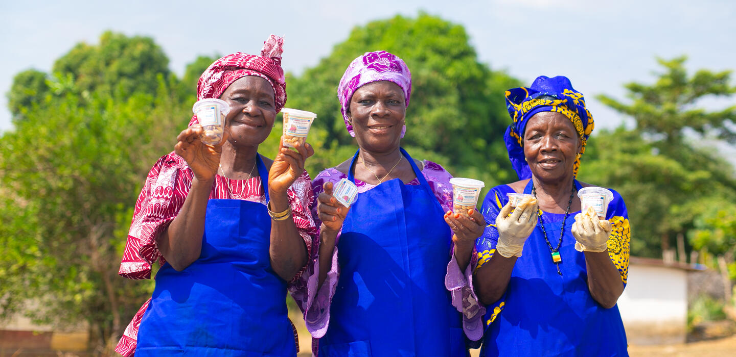 Three women employees wearing blue aprons holding cashew products.