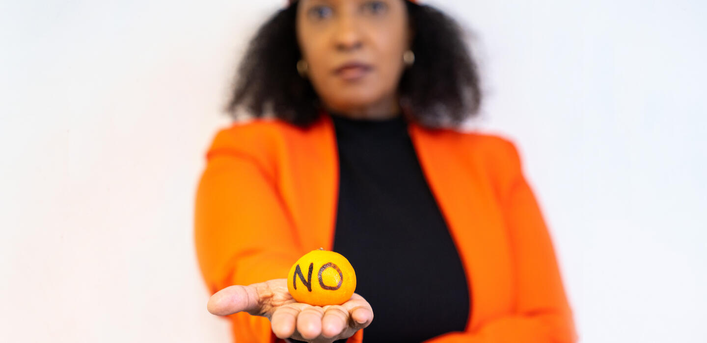 Pamela Coke-Hamilton, ED of ITC, is blurred in the background of this image, and is holding an orange clementine with the word NO written on it.