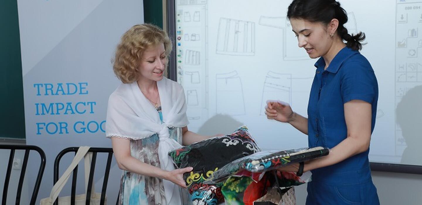 Dos mujeres mirando artesanías con un cartel del ITC al fondo