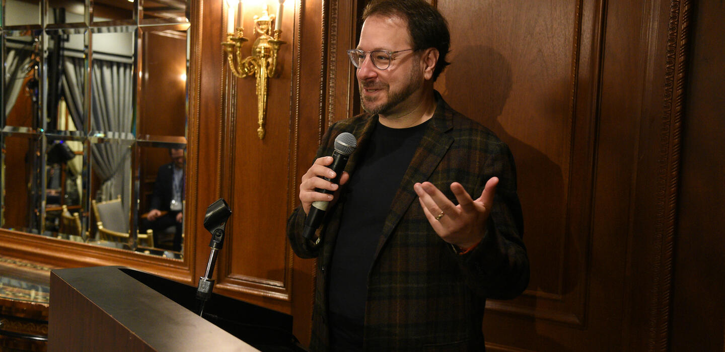 Un hombre habla en un podio en una sala y tiene un micrófono en la mano