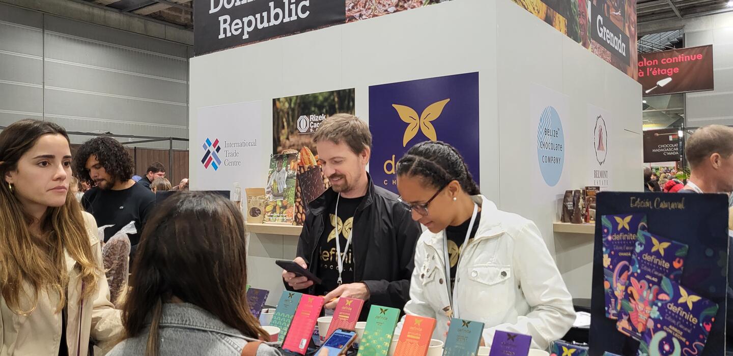 Group stands around trade fair booth showing Domincan chocolate