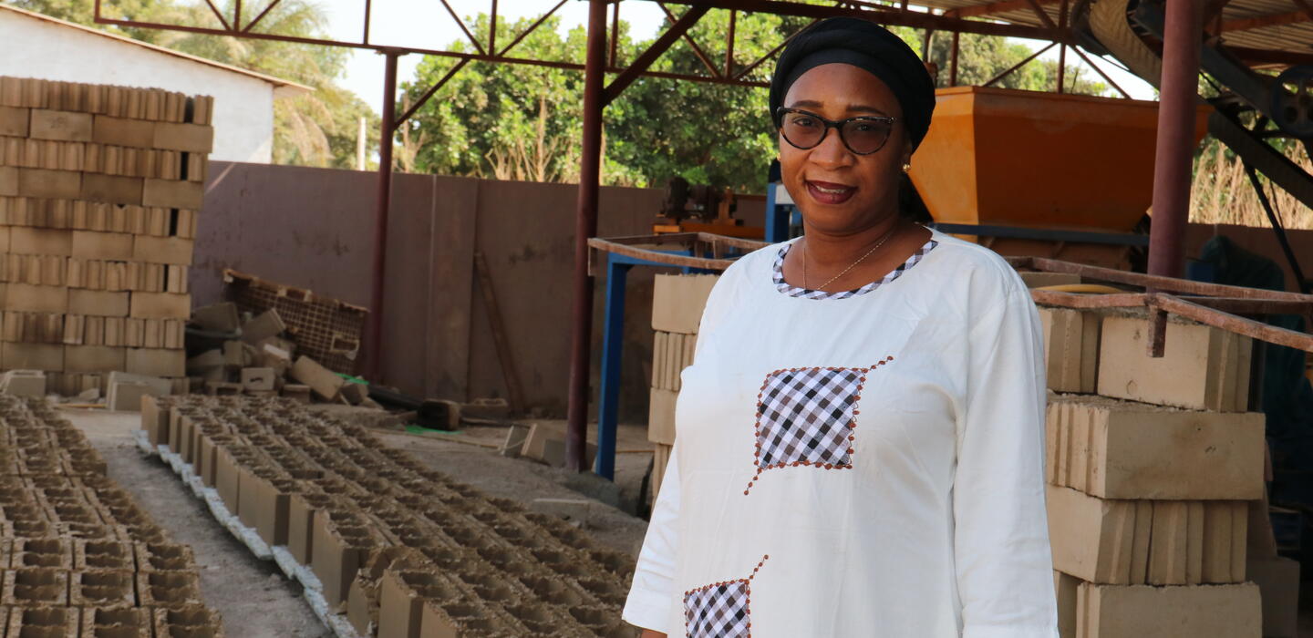 Gambian businesswoman stands next to samples of bricks made by her company