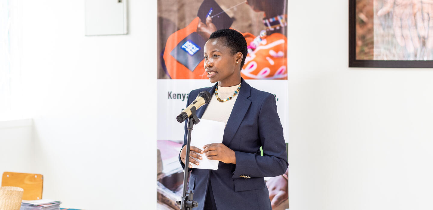 A professional woman in a suit confidently delivering a speech to an attentive audience.
