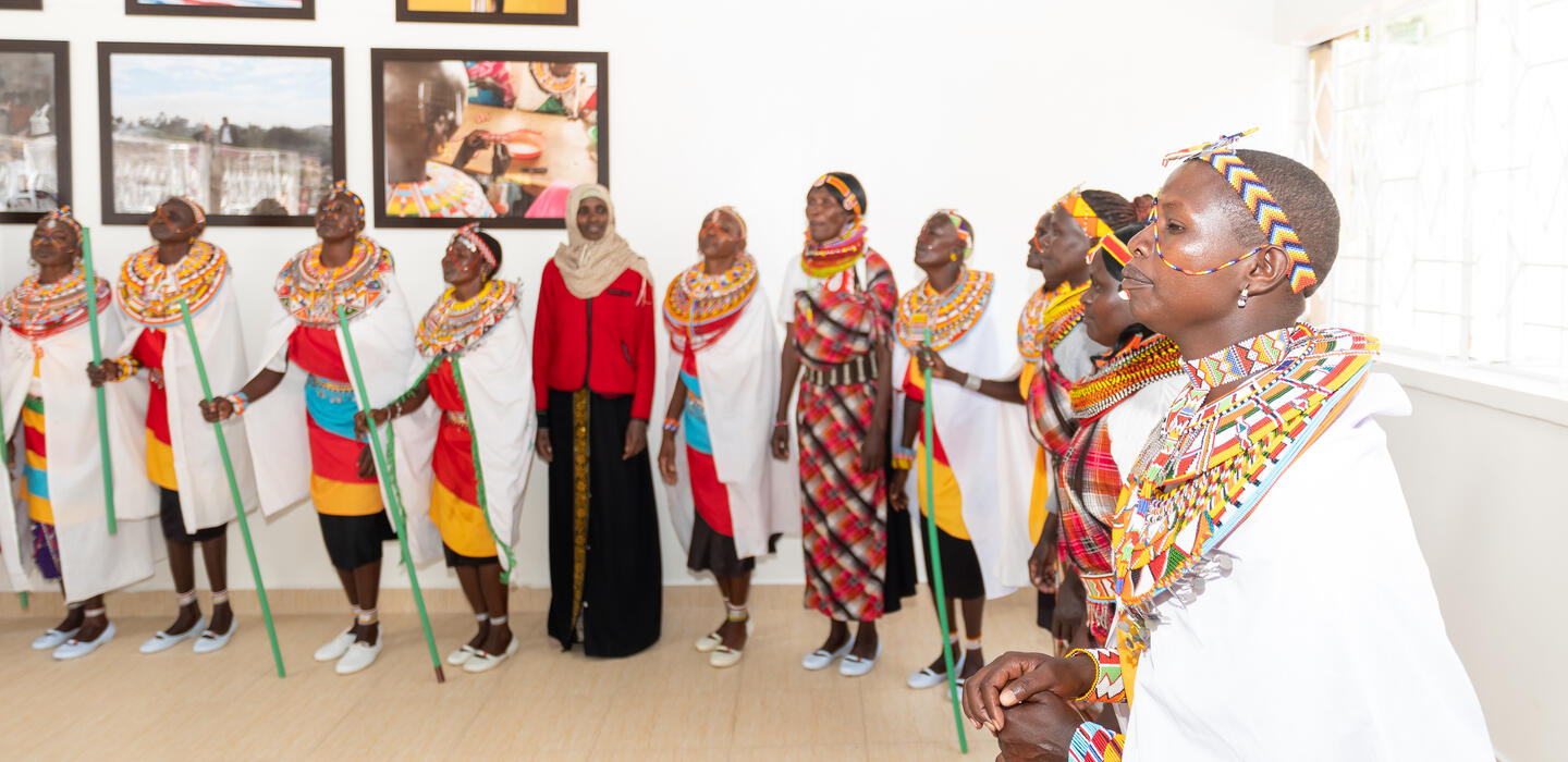Kenyan women in traditional dress stand in a well-lit room in conversation