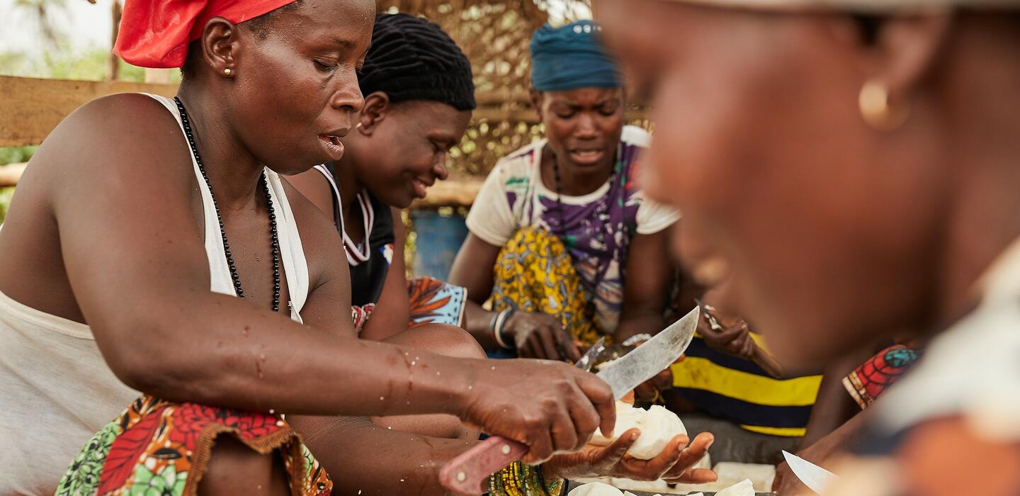Women in Sierra Leone slice cassava with a large knife