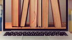 Una computadora portátil sobre una mesa que tiene una imagen de escritorio de libros de pie que muestran las páginas. El fondo es un estante de libros.