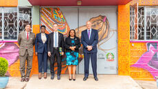 Officials in business attire stand by a wall with a brightly coloured mural